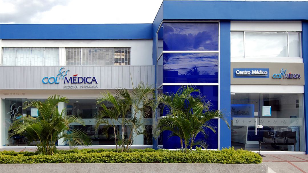 Fachada de un Centro Médico y de Diagnóstico Especializado de Colmédica en Colombia, con personal de salud recibiendo a un paciente en la entrada